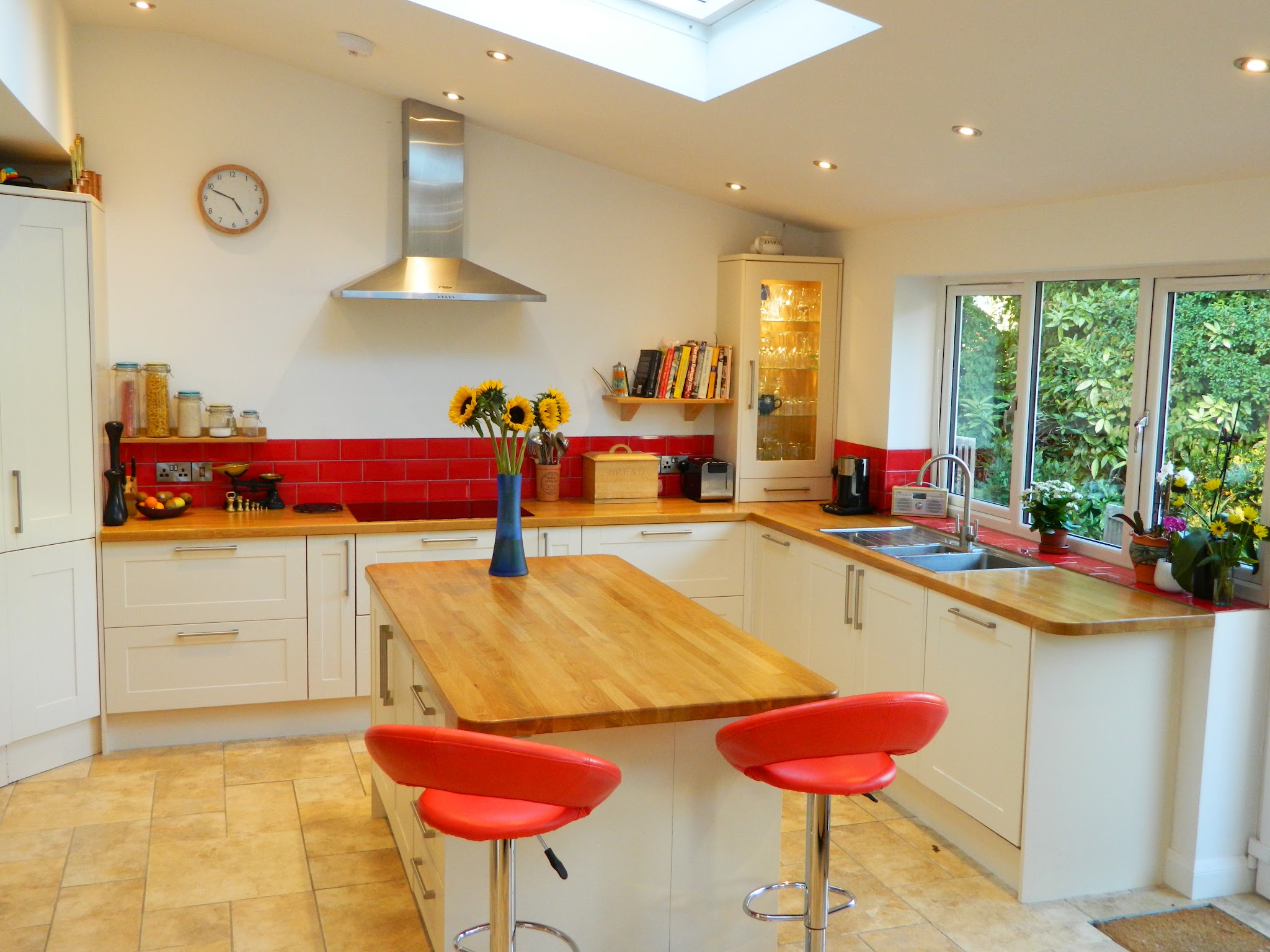 Fitted kitchen with cream units, an oak island and worktops, red bar stools and a tiled floor