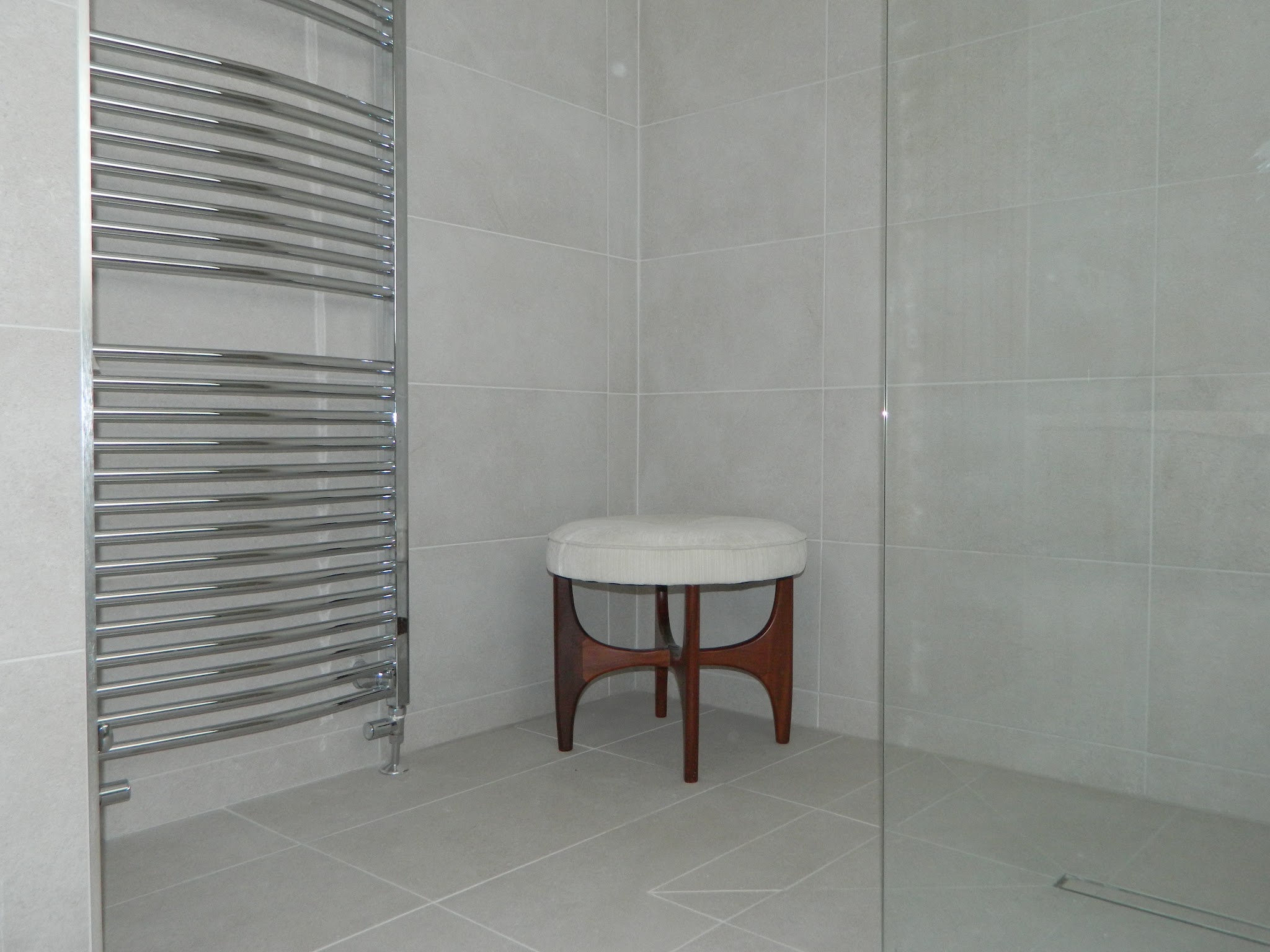 Light grey tiled wet room with a chrome towel rail and a linear floor drain