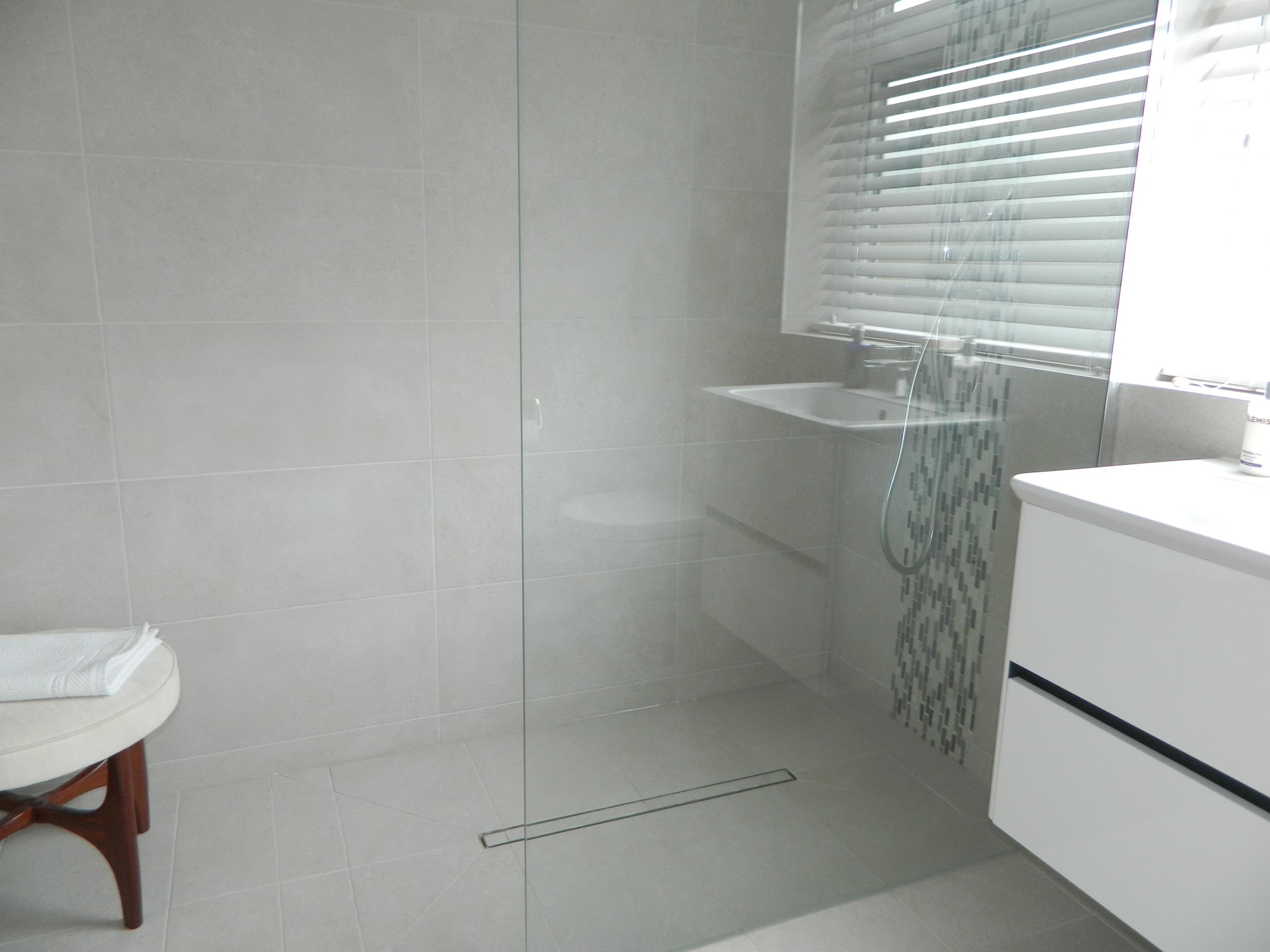 The same wet room: a frameless glass panel, a mosaic strip and a white wall-hung vanity