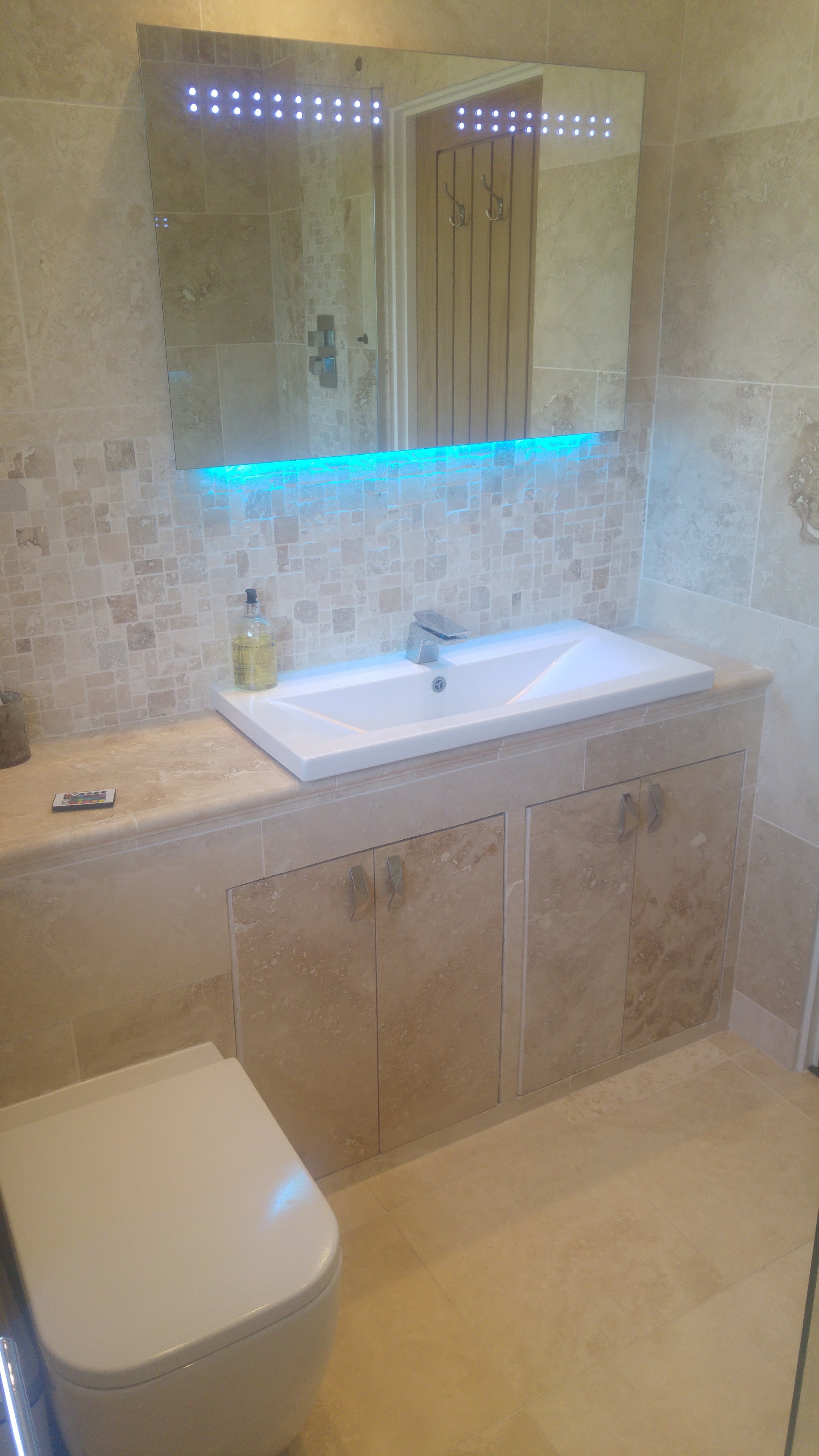 Bathroom fitted by Steve with travertine-style tiles, an LED mirror cabinet and a fitted vanity unit