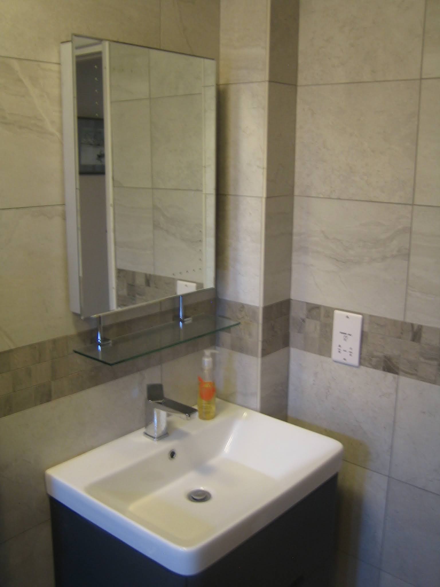 Wet room with a mirror cabinet and a white basin on a dark vanity unit, grey marble-effect tiles
